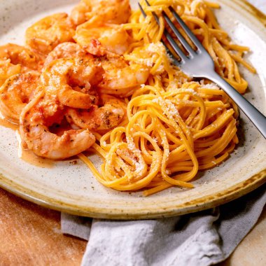 Soslu karidesli domates spagetti makarna ve kahverengi taş zemin üzerinde çatal ve bez peçeteyle servis edilen benekli seramik tabakta parmesan peyniri. Kare resim
