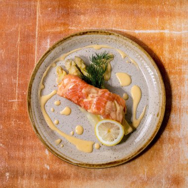 Ev yapımı seramik tabakta pişmiş somon balığı. Beyaz kuşkonmaz, limon, dereotu ve Hollandaise sosu ile servis ediliyor. Üst manzara, düz yatış. Kare resim