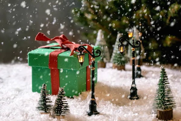 クリスマスや新年の挨拶カード おもちゃの街路灯 背景に雪やモミの木の下の周りの装飾的なクリスマスツリーと大きな緑のギフトボックス クリスマス休暇の雰囲気 — ストック写真