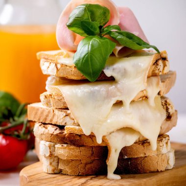 Kızarmış peynirli sandviç, jambon eti, kiraz domatesi, portakal suyu ve fesleğen yapraklı ahşap kesim tahtası. Kapatın. Kare resim