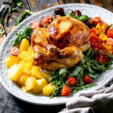 Izgara ızgara tavuk, sebze garnitürlü dolmalık biber, soğan, fırında patates, kiraz domatesleri, mantarlar ve koyu ahşap zemin üzerine seramik tabakta otlar. Kare resim