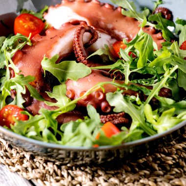 Deniz ürünleri salatası. Ahtapot ahtapot dokunaçları mavi seramik tabakta roket yaprağı aragula ve vişneli domates salatasıyla servis edilir. Kare resim