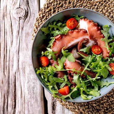 Deniz ürünleri salatası. Ahtapot dokunaçları mavi seramik tabakta roket yaprağı aragül ve vişneli salata ile servis edilir. Üst manzara, düz yatış. Uzayı kopyala Kare resim