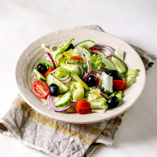 经典蔬菜沙拉与西红柿 沙拉叶和黑色橄榄在白色陶瓷盘上的布餐巾 白色大理石背景 正方形图像 — 图库照片