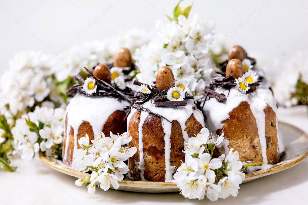 Homemade traditionla Easter cake with chocolate nests and eggs on ceramic plate and blossoming cherry tree over white background. Traditional ortodox Easter Russian Ukrainian bake. Close up