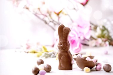 Çikolatalı tavşanlı, şekerli ve yumurtalı Paskalya tebrik kartı. Beyaz arka planda bahar çiçekleri dalları. Paskalya ziyafetleri, kopyalama alanı