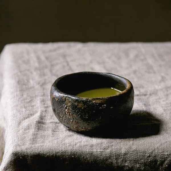 Japanese matcha green tea in wabi sabi ceramic cup with pink magnolia flowers on grey linen table cloth. Square image