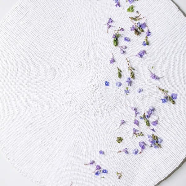 Violet purple edible flowers on white round knitted napkin over white background. Flat lay, space. Square image