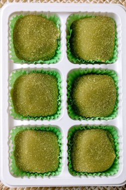 Asya pirinçli tatlı yeşil kibrit mochi perakende plastik ambalajla samandan örülmüş arka planda. Üst görünüm, kapat