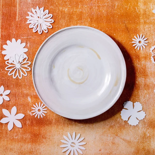 Κενό Λευκό Κεραμικό Πιάτο Χάρτινα Λουλούδια Γύρω Από Πορτοκαλί Πέτρα — Φωτογραφία Αρχείου