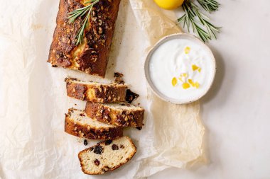 Kuru üzümlü, fındıklı ve biberiyeli dilimlenmiş limonlu kek, beyaz mermer masada taze limon ve krema beyaz sosuyla servis ediliyor. Düz yatıyordu