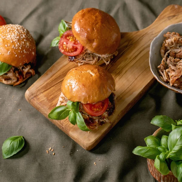 一套自制的迷你汉堡包 以炖牛肉 西红柿和罗勒配以木制切菜板和亚麻布桌布为背景 周围的杂碎和配料 现代美味的快餐 正方形图像 — 图库照片