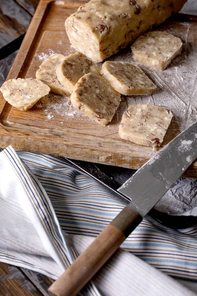 用坚果 白巧克力和厨师刀在深色木桌上的木制切菜板上切自制的小面包面团来烹调糖饼干 甜蜜的烘焙 — 图库照片