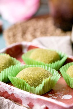 Mavi masadaki pembe seramik tabakta geleneksel Asya pirinç tatlı tatlı yeşil kibrit mochi. Arka planda bahar pembe çiçekleri.