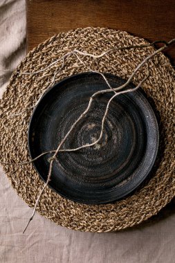 Saman peçete ve ahşap arka planda kuru dallı boş seramik tabak. Düz uzanış, boşluk.
