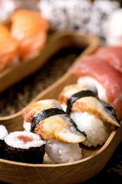 Suşi hazır. Geleneksel Japon yemeği suşisi ve taze somon, ton balığı, yılan balığı ve pirinçli karides. Kahverengi masadaki ahşap tabakta servis. Kapat.