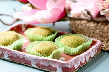 Mavi masadaki pembe seramik tabakta geleneksel Asya pirinç tatlı tatlı yeşil kibrit mochi. Arka planda bahar pembe çiçekleri.