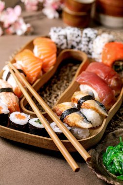 Suşi hazır. Geleneksel Japon yemeği suşisi ve taze somon, ton balığı, yılan balığı ve pirinçli karides. Kahverengi masadaki ahşap tabakta servis. Kapat.