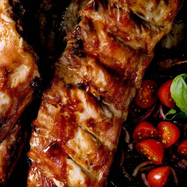 Seramik tabakta ızgara domuz pirzolası, marine edilmiş soğan, kiraz domatesleri, koyu kahverengi desenli fesleğen. Üst Manzara, kapat. Kare resim