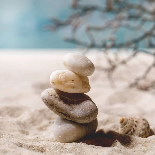 여름의 모래사장에서 파도와 껍질로 균형을 위하여 가지하얀 매끄러운 돌들을 쌓는다 — 스톡 사진