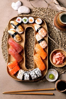 Suşi hazır. Geleneksel Japon yemeği suşisi ve taze somon, ton balığı, yılan balığı ve pirinçli karides. Kahverengi arka planda soya soslu, sake ve taşlı ahşap tabakta servis ediliyor. Düz yatıyordu.