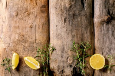 Citrus ve şifalı bitkiler. Eski ahşap arka planda taze organik dilimlenmiş limon ve biberiye dalları. Üst görünüm, boşluğu kopyala. Temel petrol konsepti