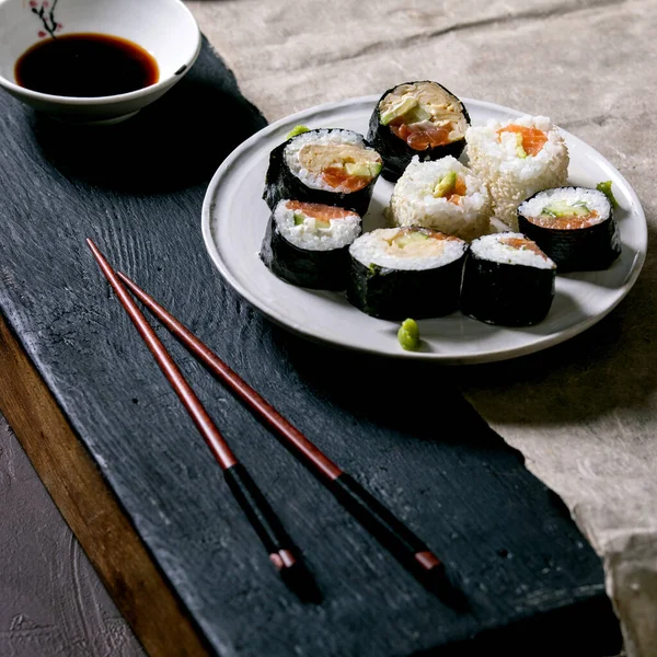 自制寿司卷 配上鲑鱼 日本煎蛋卷 芥末和酱油 配上木制筷子 盖在黑色木制桌子上 日本风格的晚餐 正方形图像 — 图库照片
