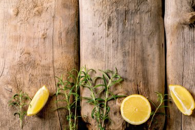 Citrus ve şifalı bitkiler. Eski ahşap arka planda taze organik dilimlenmiş limon ve biberiye dalları. Üst görünüm, alanı kopyala