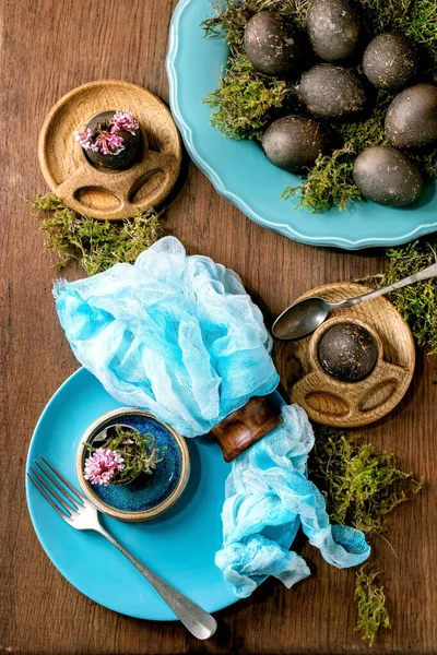 复活节餐桌设置与空绿松石陶瓷盘和蛋杯 装饰森林苔藓 黑色的彩蛋和粉红色的春花在木制桌子上 时尚的春假 平躺在床上 — 图库照片