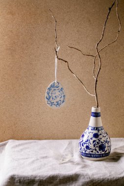 Paskalya 'nın iç mekanları. Gri el yapımı seramik porselen vazoda keten masa örtüsünün üzerinde duran kuru dallar üzerine seramik mavi yumurta boyası. Arkadaki kahverengi duvar. Boşluğu kopyala.