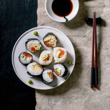 Somon, Japon omleti, avakado ve soya soslu ev yapımı suşi ruloları, siyah ahşap arka planda gri kağıt üzerinde. Japon usulü yemek. Kare resim