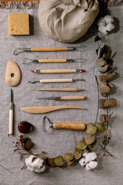 Çömlek hobisi için hazır. Çiğ gri kil ve çanak çömlek seramik gereçleri pamuklu kumaş kumaş ve okaliptüs üzerinde sıralanmış. Üst Manzara. DIY çömlekçi hobisi