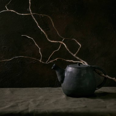 Çay seremonisi için el yapımı siyah seramik çaydanlık. Karanlık odada kuru dalla keten masa örtüsünün üzerinde duruyor. Uzayı kopyala Kare resim