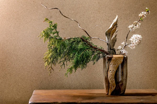 美丽的春宜家 花序与春天盛开的白花 紫杉枝条和一块木头在褐色陶瓷花瓶中 矗立在木制桌子上 日本风格的家居装饰 — 图库照片