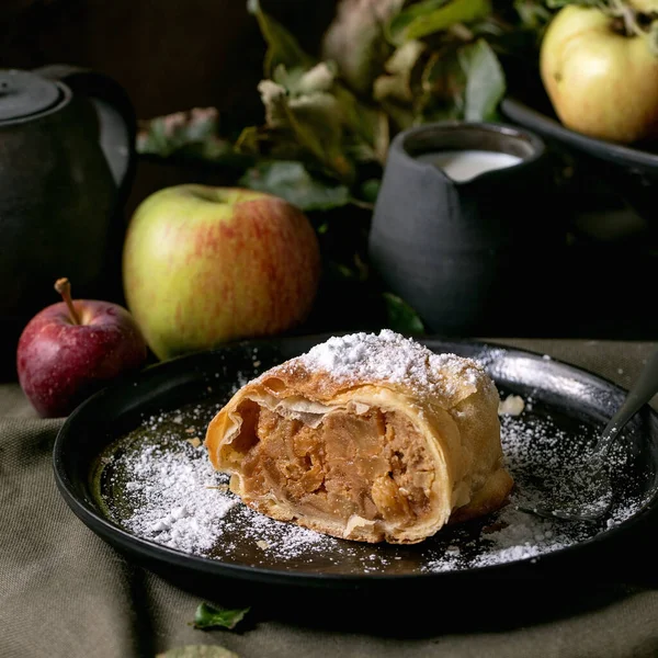 熟した新鮮なリンゴ フォーク ダークリネンのテーブルクロスでクリームを添えて黒のセラミックプレートで自家製の伝統的なアップル ストラウデル パイのスライス ダーク素朴な秋のお茶を飲む 正方形の画像 — ストック写真