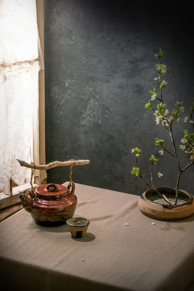 손으로 찻주전자에는 손잡이가 근처에 아마포 식탁보 위에는 의식을 장식으로 꽃나무 — 스톡 사진