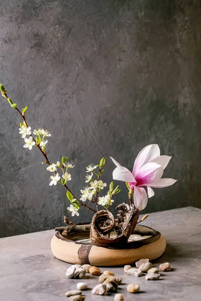 春天Ikebana 花的构图 春花盛开的木兰花和李枝花在褐色陶瓷碗里 树皮和石头围绕着 屹立在灰色的桌子上 日本风格的家居装饰 复制空间 — 图库照片