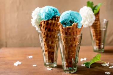 Turkuazlı dondurma, beyaz çiçekli waffle külahları, şeffaf bardaklar içinde ahşap masada duruyor. Moda ev yapımı yaz tatlısı. Boşluğu kopyala