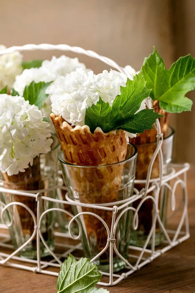 自制的甜松饼圆锥 白色的花和绿色的叶子 站在木制桌子透明的眼镜上 夏天自然花糖甜点的概念 靠近点 — 图库照片