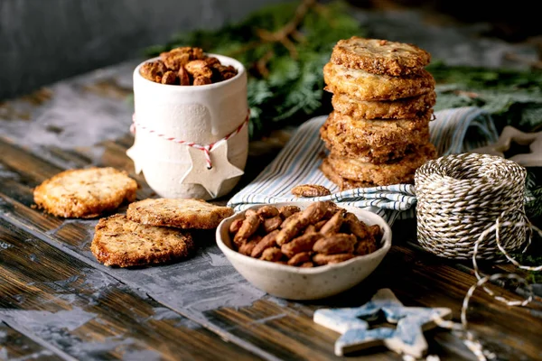 クリスマスのシンプルな甘い手作りの贈り物 暗い木製のテーブルの上にクリスマスの装飾が付いている釉蜂蜜ローストアーモンドナッツと正方形のショートブレッドシュガークッキーのボウル お菓子 ストック写真