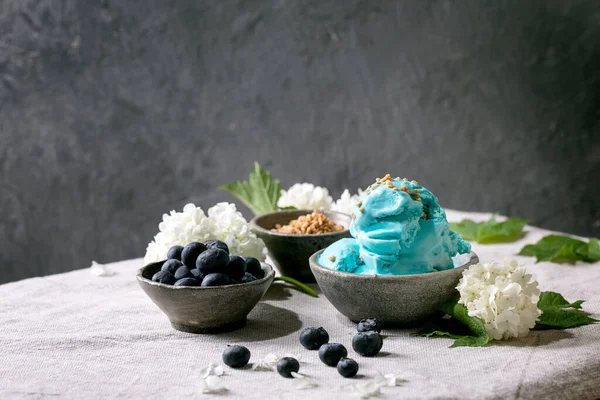 陶瓷碗里的自制绿松石冰淇淋 蓝莓和白花 站立的灰色亚麻布桌布 时尚的自制夏季甜点 复制空间 免版税图库图片