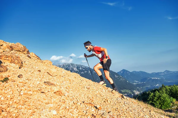 山で石の斜面を登る若い男が棒で押す — ストック写真