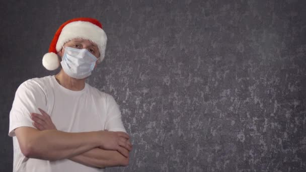 Noel Baba şapkalı ve yüzünde tıbbi maske olan bir adam. Noel ve koronavirüs. — Stok video