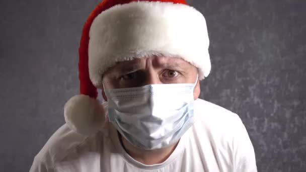 Noel Baba şapkalı ve yüzünde tıbbi maske olan bir adam. Noel ve koronavirüs. — Stok video