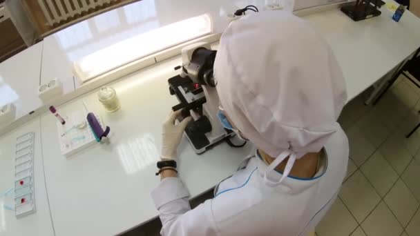 O femeie medic efectuează cercetări medicale folosind un microscop. — Videoclip de stoc