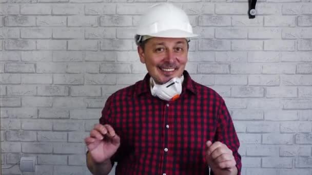 Um construtor feliz no fundo de uma parede de tijolos está dançando e aproveitando o momento. — Vídeo de Stock