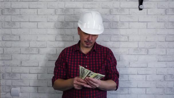 Portret wesołego człowieka w kasku budowlanym rzucającego pieniędzmi. Na tle murowanej ściany . — Wideo stockowe