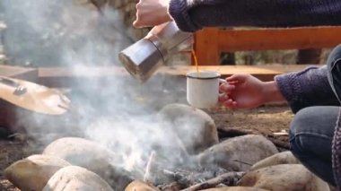 Gezgin kadın şenlik ateşinin yanına sıcak kahve koyuyor.