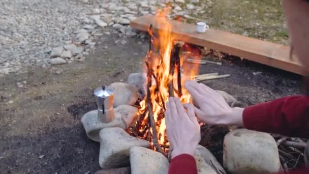 Samec, který si ohřívá ruce ohněm, je obklopen lesem. Aktivní turistika venku — Stock video