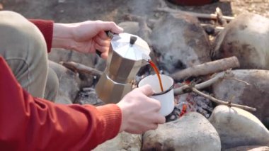 Kampın yanındaki sandalyede oturan ve bir fincan kahve içen bir adam.. 